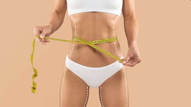 Dieting Concept. Unrecognizable Female In Underwear Checking Waist Size With Measuring Tape