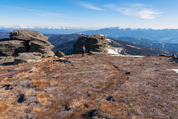 Rear view of woman with backpack hiking on snow covered alpine meadow to Steinerne Hochzeit, Saualpe, Lavanttal Alps, border Styria Carinthia, Austria, Europe. Panorama of snowcapped mountain range
