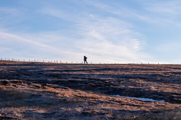 Silhouette of a woman hiking on alpine meadow along a fence after sunrise from Ladinger Spitz to...