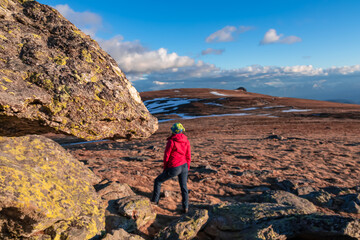 Fototapeta premium Woman with ear flap hat standing on alpine meadow with scenic view on Grosser Sauofen (Ebersteiner Sau), Saualpe, Lavanttal Alps, Carinthia, Austria, Europe. Rock formation in the foreground