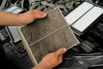 A new car air filter and an old one with garbage in the hands of a man. Comparison and preventive replacement in the car.