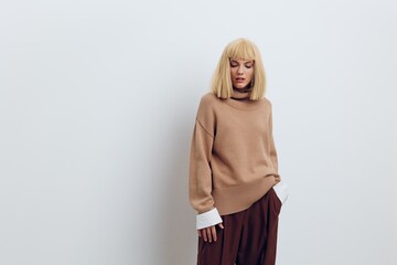 Fototapeta premium Horizontal photo, a woman on a white background in a beige sweater and brown trousers with beautiful blond hair is standing