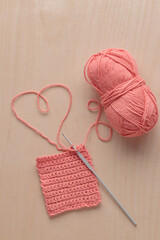 Heart Shaped Yarn and Crochet handmade square pattern, pink yarn coil, hook, knitting crocheting top view on a wooden background