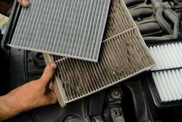 A new car air filter and an old one with garbage in the hands of a man. Comparison and preventive...