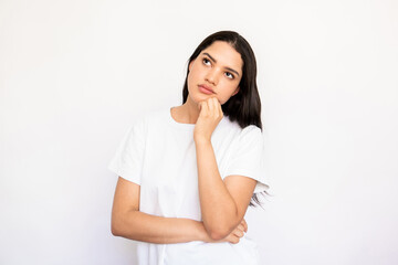 Portrait of confident young woman thinking over idea. Caucasian lady wearing white T-shirt standing with hand on chin and looking away over white background. Thinking or planning concept