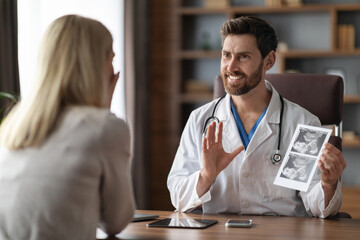 Smiling Gynecologist Doctor Showing Baby Sonography Image To Pregnant Female Patient