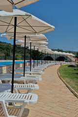 Sun loungers and sun umbrellas along the path in the park. Summer holidays in a closed area with a swimming pool