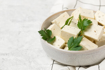 Tofu soy cheese or paneer or feta cheese cubes adding fresh parsley and celery in a ceramic bowl on...