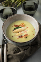 Delicious closeup view of a chunky asparagus soup bowl next to two water glasses over an elegant dinner table.
