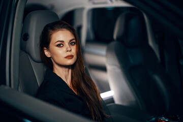 a stylish, luxurious woman is sitting in a black car at night in the passenger seat, looking at the camera in a relaxed way. Topics of safe driving on the roads