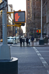Metal pole on a new york corner with red hand lighted sign of no crossing the street, with blurred people in the background