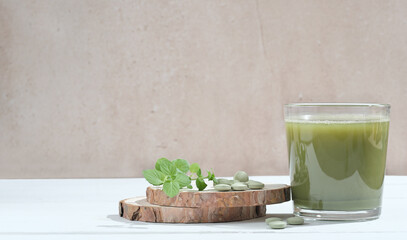 Healthy spirulina drink in the glass with spirulina chlorella tablets on tree saw cut podium. Superfood, detox drink. Health care, antioxidant drink. copy space