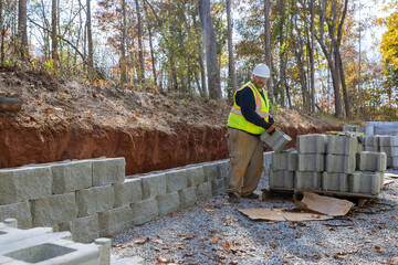 Man uses leveling tool during construction of concrete block wall to create retaining wall on new property