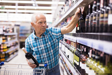 elderly retired senor buying wine in the alcohol section of the supermarket