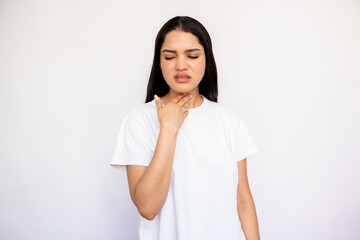 Portrait of unhappy young woman feeling pain in throat. Caucasian lady wearing white T-shirt touching neck over white background. Pulmonary diseases concept