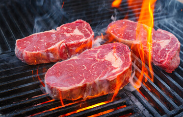 Barbecue dry aged angus rib-eye beef steak grilled as close-up on a charcoal grill with fire and...