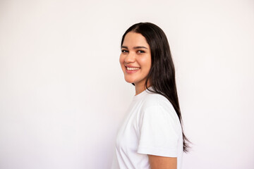 Portrait of candid young woman looking at camera and smiling over white background. Caucasian lady wearing white T-shirt posing in studio. Female beauty concept