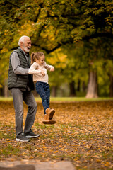 Grandfather spending time with his granddaughter in park on autumn day