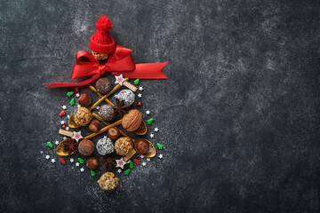 Christmas tree made of chocolate truffles, hazelnuts, anise stars, decorations, spoons and powdered sugar snow on dark background. Christmas holiday card. Holiday food concept for magazine page.