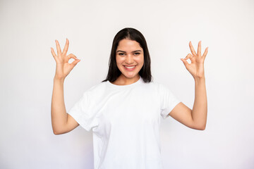 Portrait of happy young woman making ok gesture over white background. Caucasian lady wearing white...