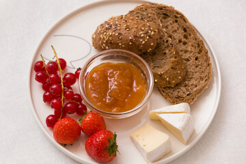 Whole grain bread, cheese, apricot jam, red currants and strawberries on a plate. Healthy breakfast