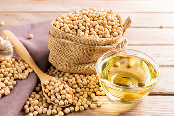 Soybean oil in a glass bowl and soybean seeds in sacks with a wooden spoon placed on a wooden table...