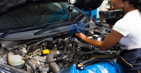 Fototapeta na wymiar African female auto mechanic worker checking oil level in car engine at Car Service station. Car maintenance and auto service garage concept.