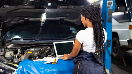 African female Professional car mechanic repair service and checking car engine by Diagnostics Software computer. Expertise mechanic working in automobile repair garage.