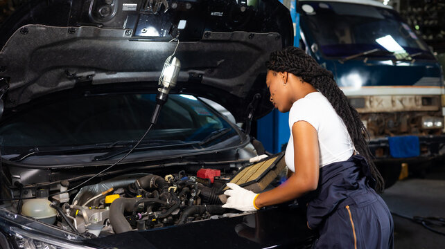 African young female car mechanic checking and changes car air filter engine at service car garage. Black woman mechanic working in car service and maintenance workshop.