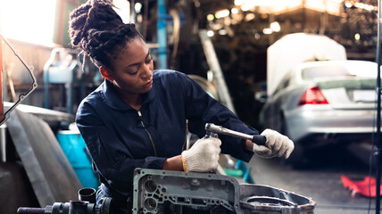 African young female car mechanic checking and fixing car engine at service car garage. Black woman mechanic working in car service and maintenance workshop.