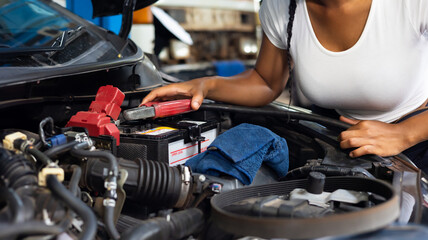 Charge electric power to ca battery by charging jumper cables. African  mechanic female uses ...