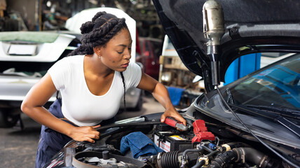 Charge electric power to ca battery by charging jumper cables. African  mechanic female uses  multimeter voltmeter to check voltage level in car battery at car service and maintenance garage.