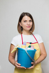 The girl holds a bucket and cleaning products in her hands