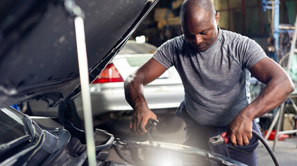 African american mechanic man uses  multimeter voltmeter to check voltage level in car battery at...