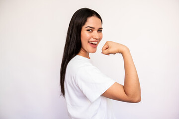 Fototapeta premium Portrait of happy young woman showing muscle on white background. Caucasian lady wearing white T-shirt showing fit body. Strength and fitness concept