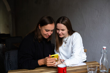 Two young women communicate and look into smartphone in cafe on terrace