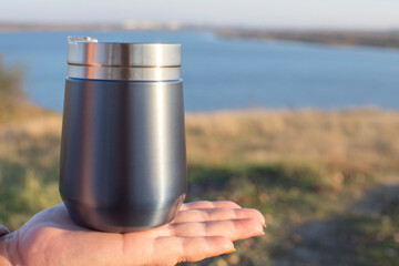 A travel mug in the hands of a girl. Picnic and party with drinking in outdoor.