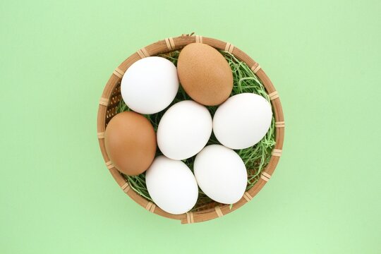 Fresh chicken eggs in wooden rattan wicker basket on green background. Natural healthy nutrition organic farm food product concept. World egg day, easter holiday composition. Close-up, flatlay