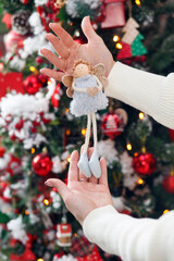 Christmas angel in hands. Christmas, New Year interior with garland, red and gold balls on a fur tree background