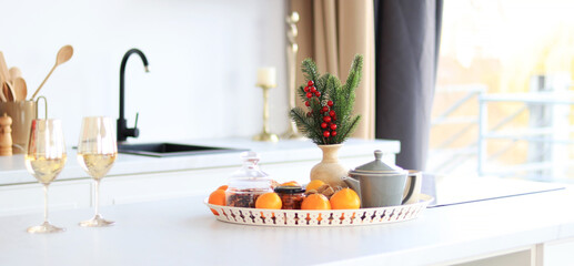 Still life of tangerines, teapot and scales with spruce branch on kitchen table, bright sunny interior. Festive atmosphere in the kitchen, selective focus