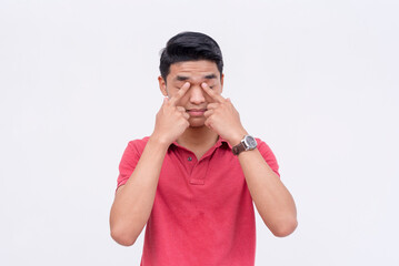 A teary eyed young man wipes some tears with his fingers. Isolated on a white background.