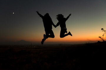 Fototapeta na wymiar Silhouette of a couple jumping against the sky during sunset