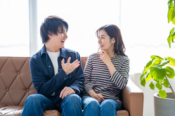 ソファに座り会話する夫婦-明るい観葉植物のあるリビング