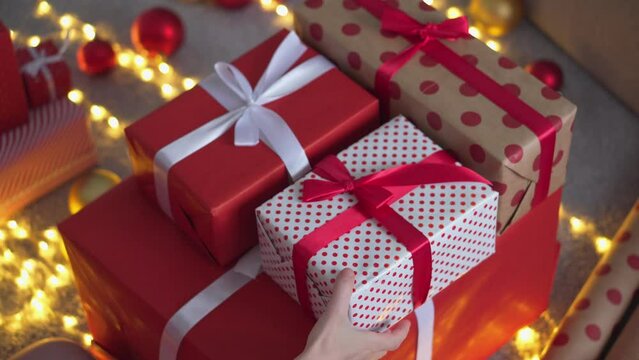 Girl in a Santa hat creates New Year's packages from red wrapping paper. Young woman is packing Christmas presents for her friends and relatives. Decorations, preparation for the winter holiday season