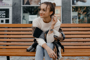 Girl sitting on a wooden bench, outdoors. Young stylish girl in a scarf and black coat sitting on a bench.