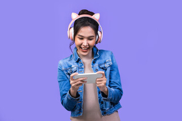 Beautiful Asian young woman in jacket jean and playing video games using joysticks with headphones on voilet background isolated. © anon