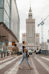 Beautiful girl in the city. The girl looks at the streets of the Warsaw. Stylish woman walks on the street on background of the Palace of Culture in Warsaw. Concept of polish lifestyle and travel.
