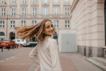 Fototapeta premium Close-up portrait of laughing brunette girl in beige sweater on city background. Woman posing.