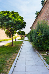Fototapeta premium Green garden with clean grass, beautiful trees, alleys in a fortress yard. The fortification walls and promenades in Alba Iulia, Romania, 2021