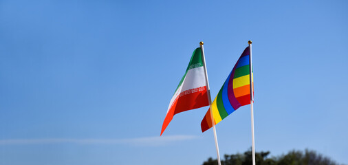 Iran national flag and rainbow flag stand together against bluesky background, concept for lgbt celebration and respecting gender diversity of human in Iran, soft and selective focus.